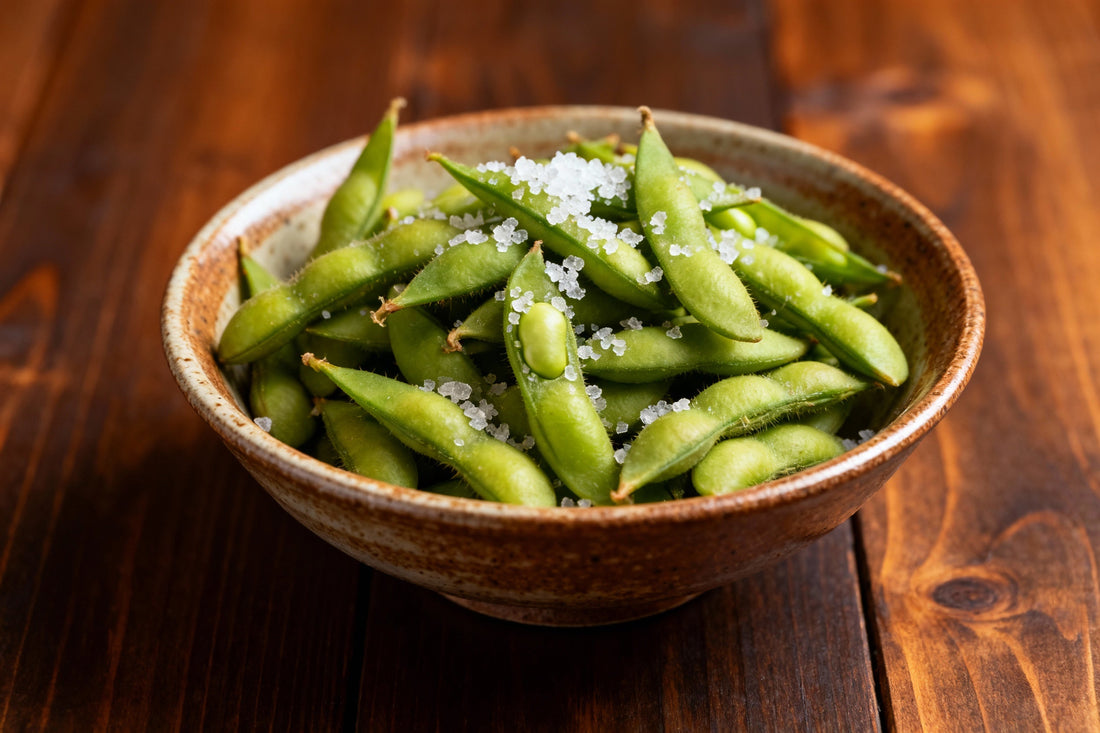 Frisch zubereitete Edamame-Schoten in einer rustikalen Schale mit Meersalz bestreut, serviert auf einem dunklen Holztisch – symbolisiert gesunde Ernährung, asiatische Herkunft und modernen Lifestyle-Snack.